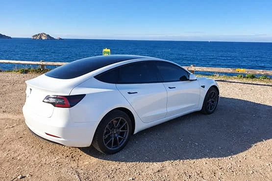 Tesla blanche vue de trois quarts arrière, stationnée face à la mer.