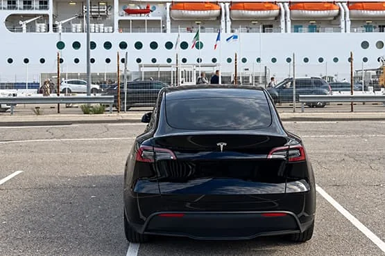 Tesla noire vue de l’arrière devant un paquebot à quai.